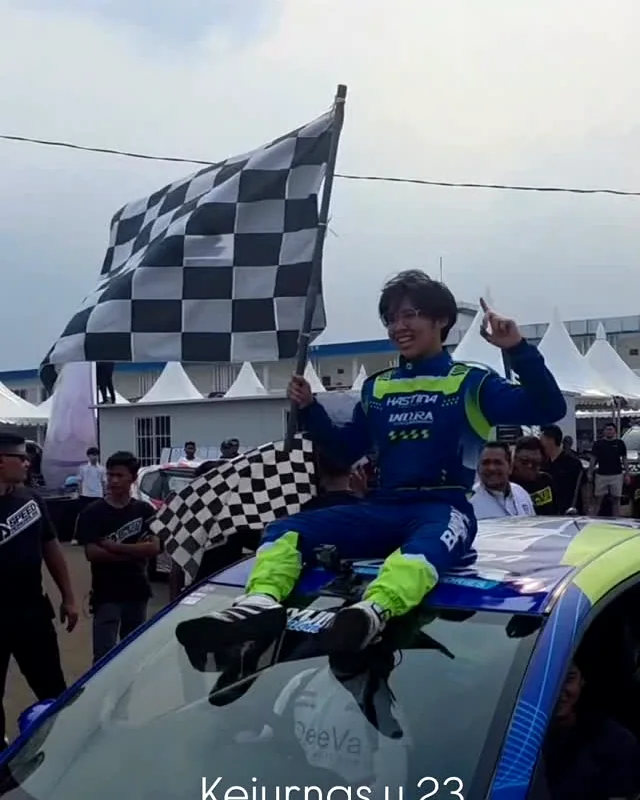 Pembalap berpose dengan bendera kotak-kotak di atas mobil tim