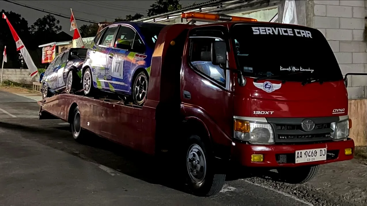 Mobil balap tim diangkut dengan truk servis menuju venue lomba